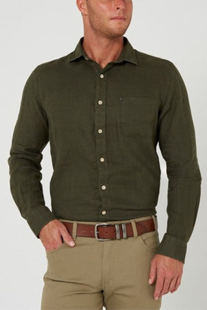 A man wears an olive green Pilbara Linen Shirt (100% linen), tucked into light brown pants with a brown belt, standing against a plain light background. His left hand is in his pocket and his right arm rests casually by his side.