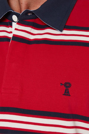 Close-up of the Pilbara Rugby Jersey, a red 100% cotton polo with white and navy horizontal stripes, a small windmill chest logo, and a navy collar with a white button, inspired by classic rugby designs.