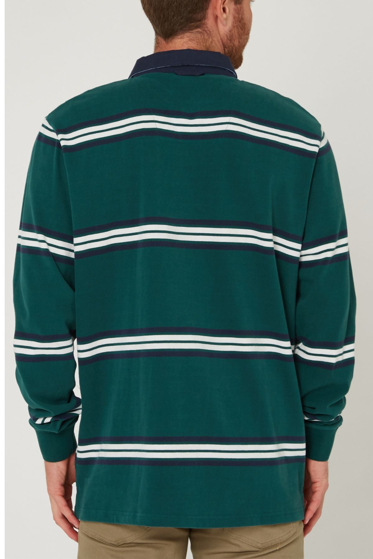 A man is shown from the back wearing a green Pilbara Rugby Jersey made from 100% cotton with horizontal white and navy stripes, a navy collar, and paired with beige pants.
