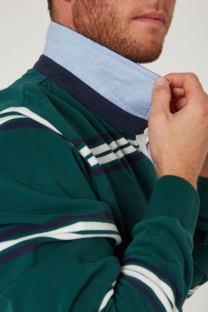 Wearing the Pilbara Rugby Jersey in green and blue stripes, made from 100% cotton, someone adjusts a light blue detachable collar. Only their lower face and upper chest are visible.