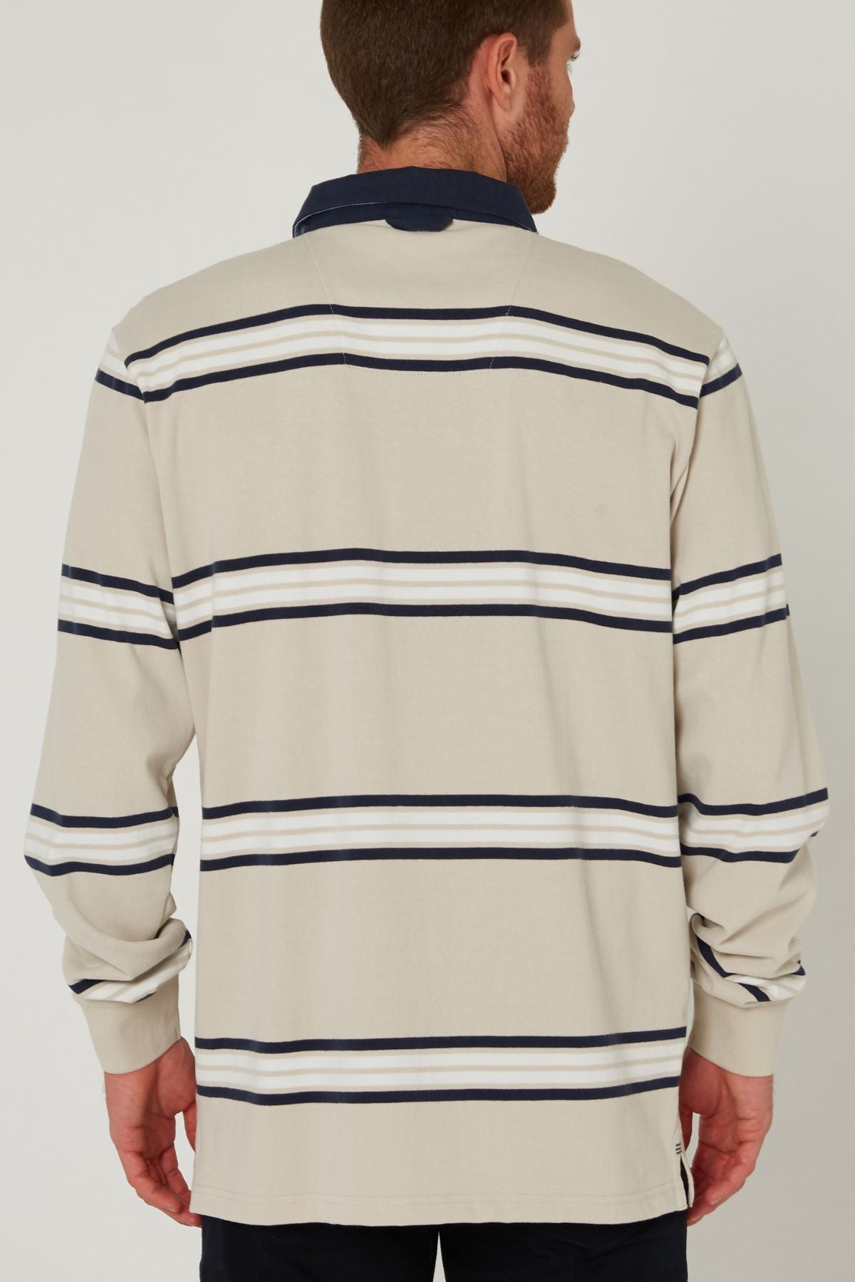 A man is seen from behind wearing a beige Pilbara Rugby Jersey with navy blue and white horizontal stripes and a dark collar, standing against a plain background.