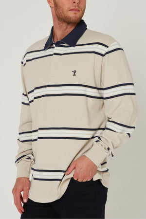 A man wearing a Pilbara Rugby Jersey in beige with navy and white horizontal stripes and a navy collar, standing with one hand in his pocket.