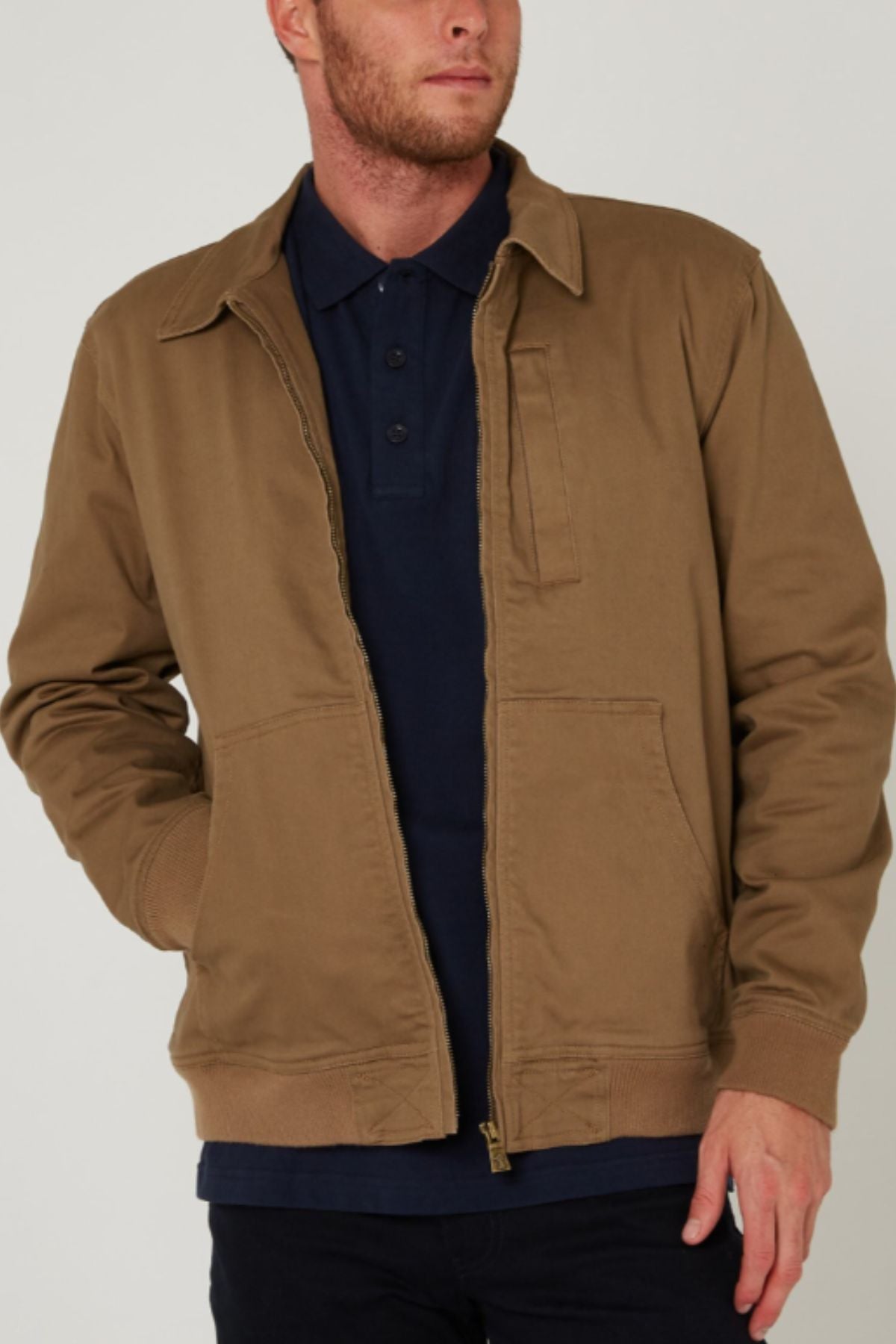 A man wears a Pilbara Sherpa Bomber Jacket over a navy blue polo shirt, standing with one hand in his pocket against a plain background.