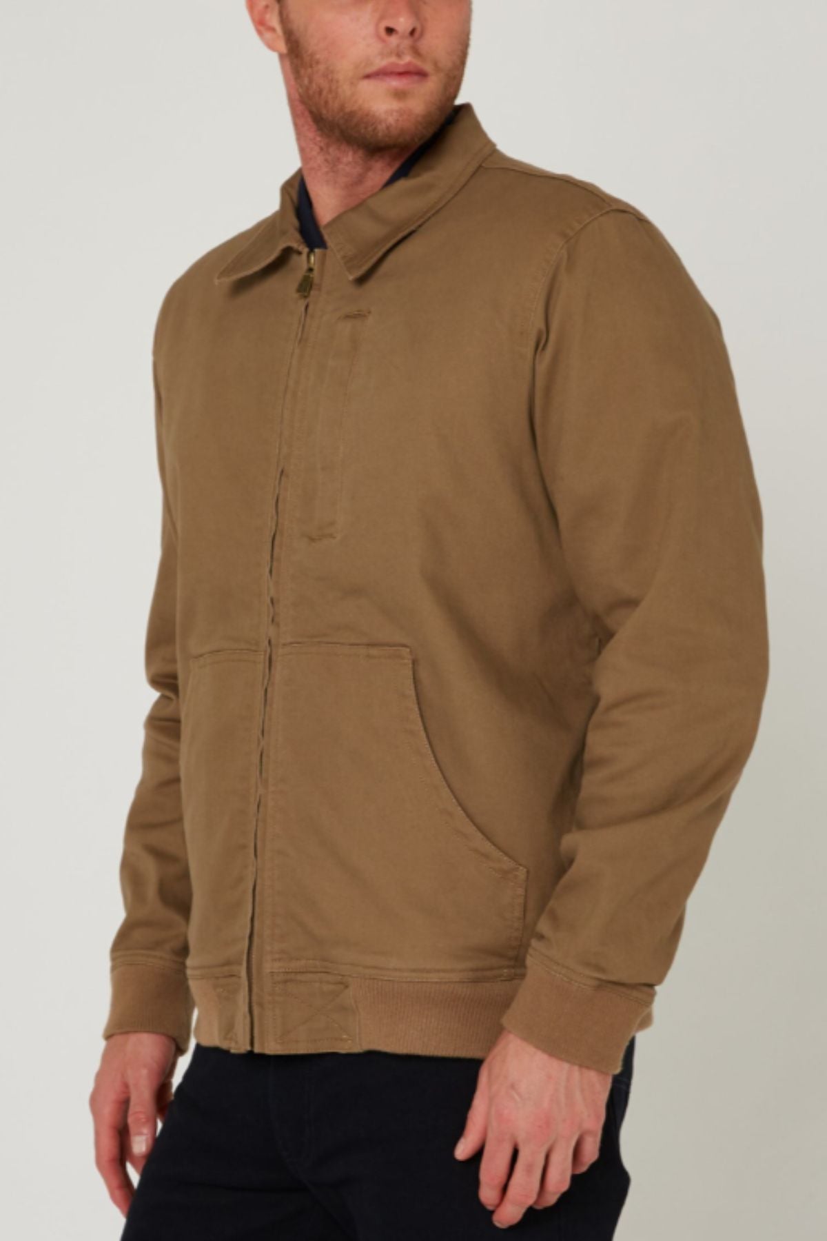 A man stands slightly turned against a plain light background, wearing a Pilbara Sherpa Bomber Jacket with front pockets and black pants.