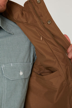 A person opens a Pilbara Two Tone Vest to reveal its inside pocket; they are wearing a green and white checkered shirt with a buttoned chest pocket.