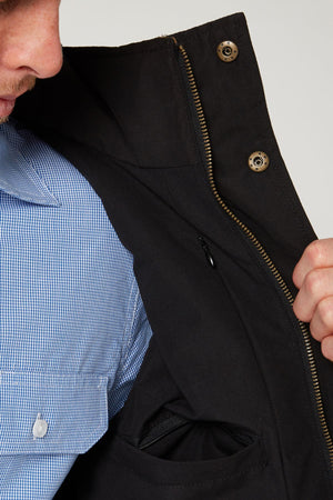 A person in a blue checkered shirt opens the Pilbara Two Tone Vest, revealing its inner pocket and zipper details, with only the lower part of their face visible.