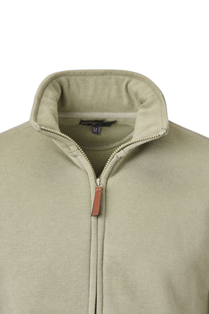 Close-up of a light olive green Pilgrim Full Zip Fleece with a standing collar. The zipper is partly open, showing a brown pull tab and a black size “M” tag.