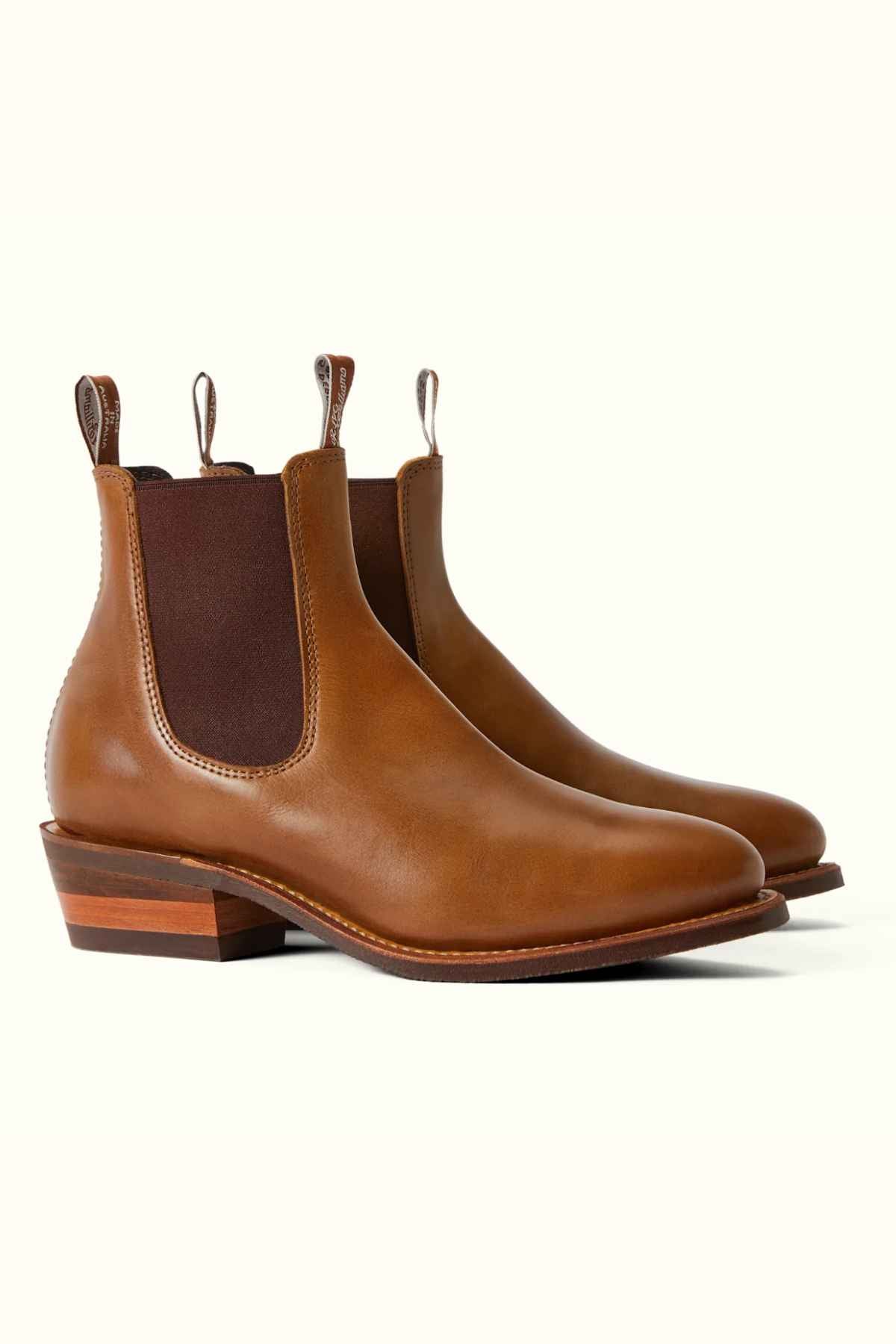 The RM Williams Comfort Lady Yearling Rubber Sole Boot, crafted in Australia, showcases brown leather with elastic side panels, pull tabs at the back, and a sturdy wooden heel. Angled images reveal both side and front views against a light background, promising style with every step.