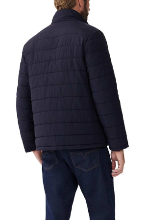 A man faces away, wearing the RM Williams Patterson Creek Jacket— a dark quilted zip-through made from recycled nylon— with dark blue jeans, set against a white background.