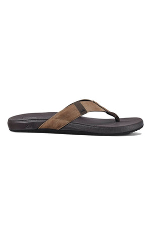 The REEF Cushion Phantom flip-flop, with a brown and black design, features a fabric strap and slightly textured footbed on a plain white background. Renowned for comfort, its sleek and casual style ensures durability for daily use.