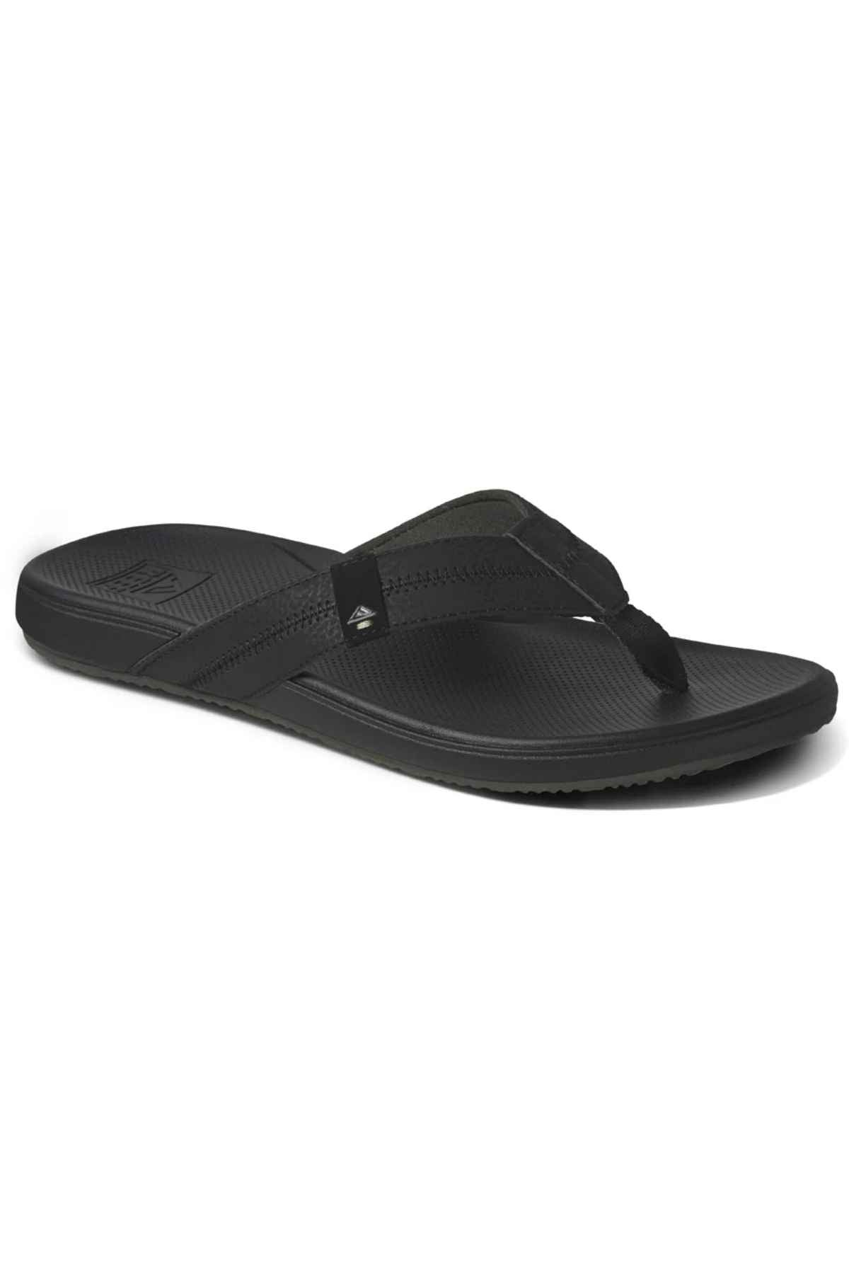 The REEF Cushion Phantom 2.0 is a black flip-flop sandal with a textured footbed, wide straps, and a low-profile sole that provides arch support for all-day wear, shown angled on a plain white background.