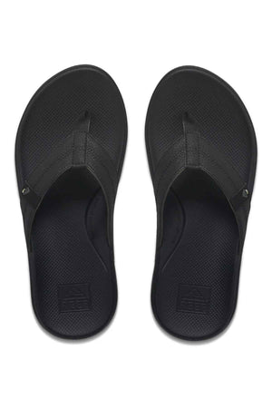 A pair of black REEF Cushion Phantom 2.0 flip-flops with textured footbeds and wide straps, shown from above on a white background. The REEF logo appears on the heel, and these sandals are designed for all-day comfort.