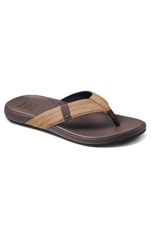 The REEF Cushion Phantom 2.0 is a brown flip-flop sandal featuring a textured sole, two-tone dark brown and tan strap, and a molded rubber outsole for durability, shown on a white background.