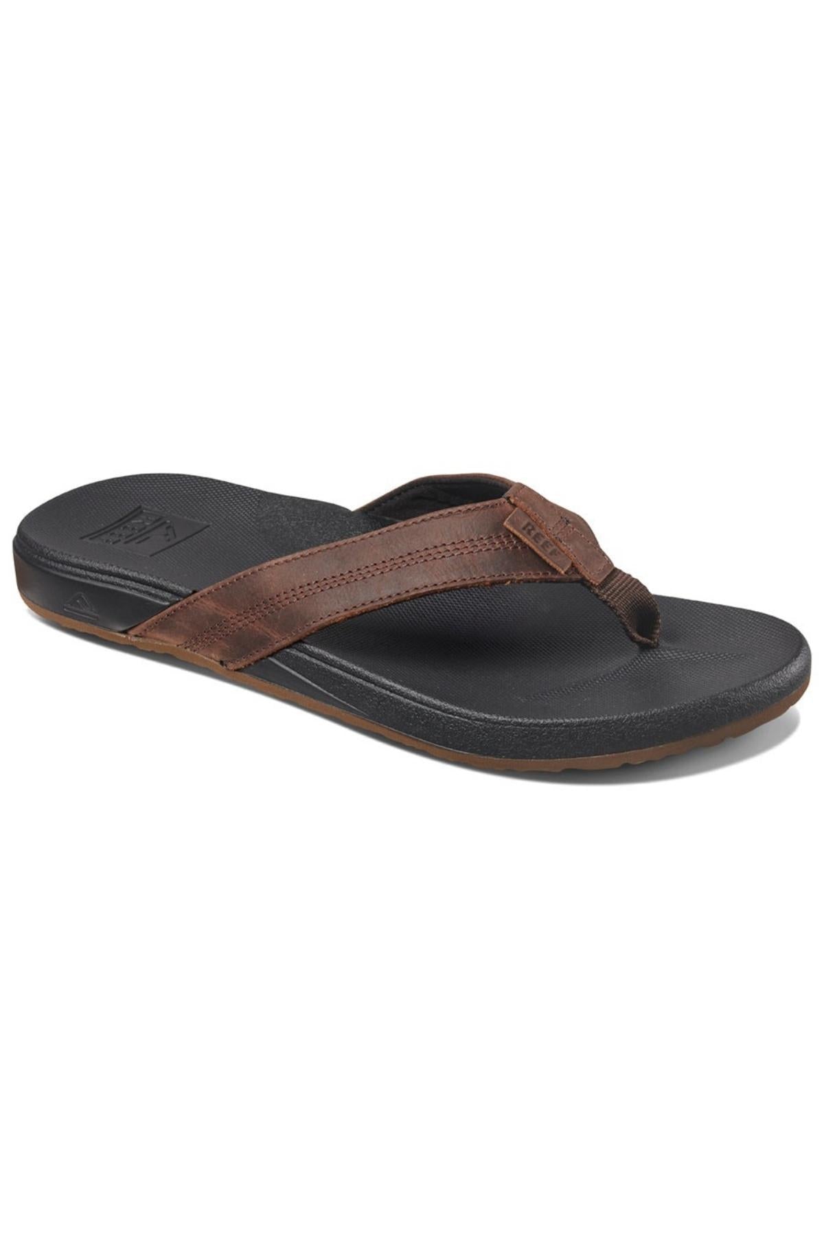 The REEF Cushion Phantom LE is a brown and black thong flip-flop sandal with a thick leather strap, textured rubber sole, and cushioned footbed, displayed at an angle on a white background.