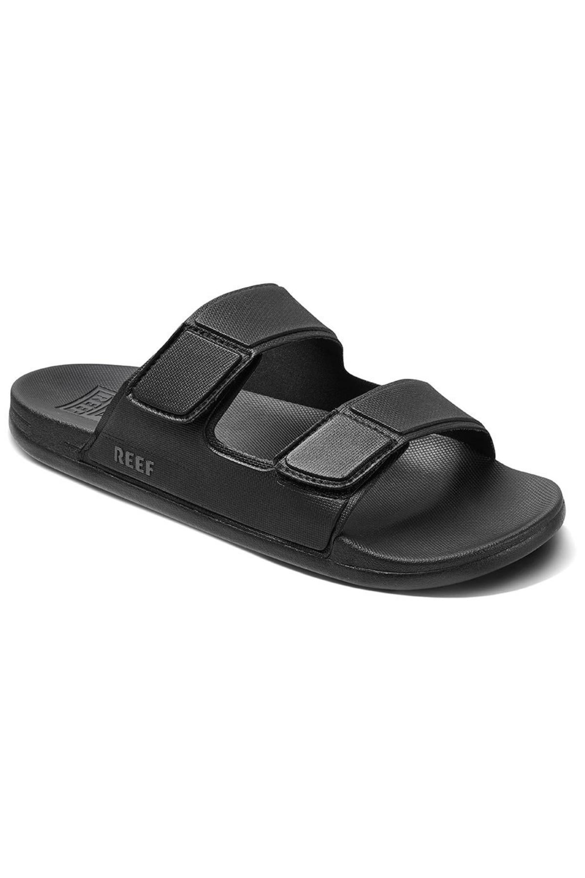 A black REEF Cushion Tradewind sandal featuring two adjustable Velcro straps, a textured cushion footbed, and "REEF" printed on the side of the sole.