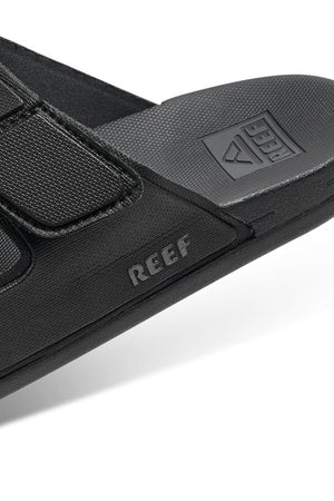 Close-up of the black REEF Cushion Tradewind sandal featuring a textured strap, "REEF" branding on the side, and logo on the cushioned footbed. The sandal offers a casual, sporty look.