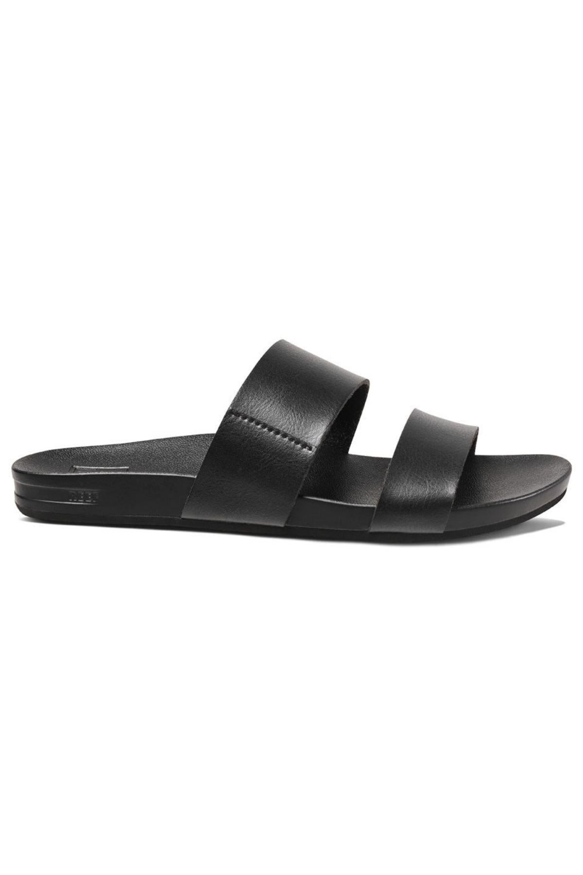 The REEF Cushion Vista is a black slide sandal with two wide vegan leather straps across the top and a flat sole, designed for casual wear. Featuring a cushion bounce midsole, this minimalist sandal is perfect for both indoor and outdoor use.