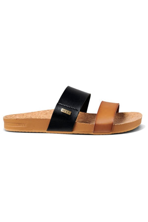 The REEF Cushion Vista Duo sandal includes a flat cork sole, two wide straps—brown front and black back with a small label—and a light tan footbed that offers cushion bounce for comfort, creating a casual and stylish appearance.
