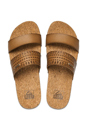 The REEF Cushion Vista Perforated sandals feature two brown leather straps per sandal, cork soles, plain top straps, lower straps with small triangular cutouts, built-in arch support for added comfort, and "REEF" embossed on the soles.