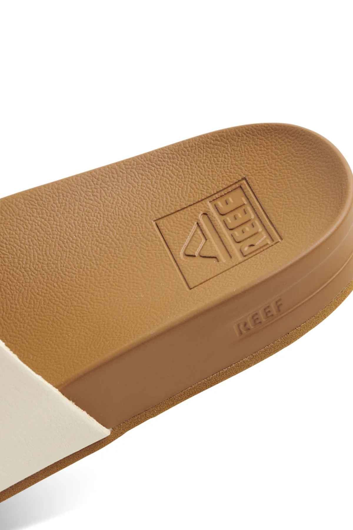 Close-up of REEF Cushion Vista in brown, with brand name and logo on the sole. Image shows part of the textured memory-free foam footbed and heel for arch support, along with the edge of a white strap.