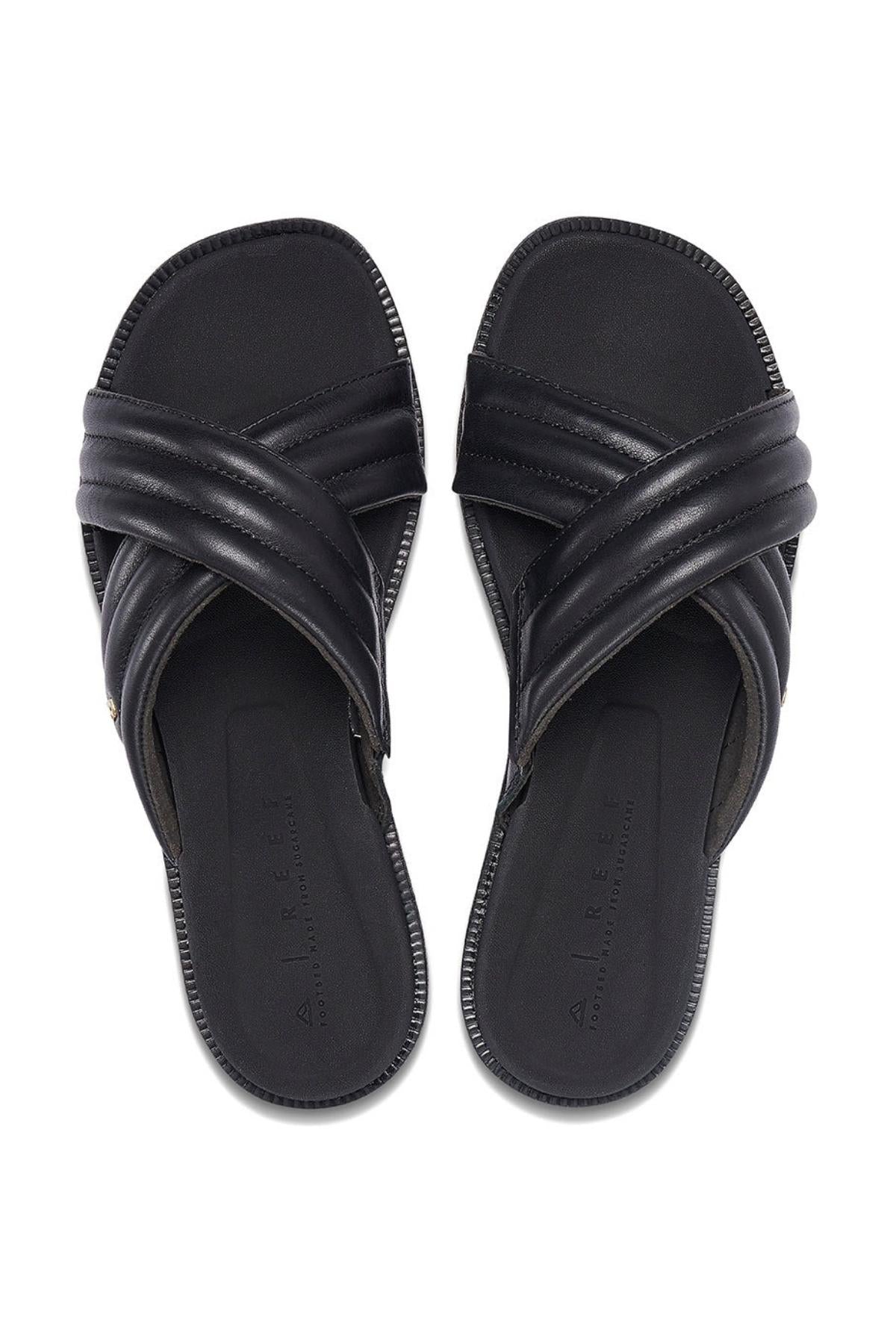 A pair of REEF Lofty Lux X black slip-on sandals with crisscross padded straps and open toes, shown on a white background—ideal for anyone seeking premium comfort and sustainable style.