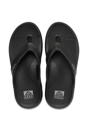 A pair of REEF Oasis sandals in black, featuring textured footbeds and the Reef logo on both the heel area and straps, are made with renewable sugarcane EVA for reliable arch support. These flip-flops are placed side by side, facing upward on a white background.