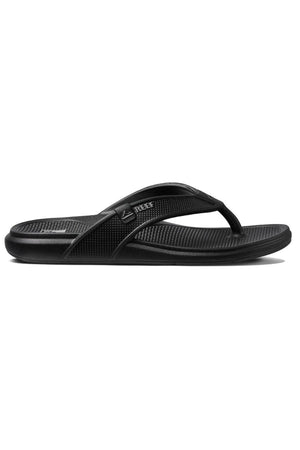 The REEF Oasis sandals are black flip-flop sandals with a textured footbed, a simple thong strap design, and the brand logo "REEF" displayed in white. These sandals feature arch support, a contoured footbed for added comfort, and are made from renewable sugarcane EVA for an eco-friendly touch.
