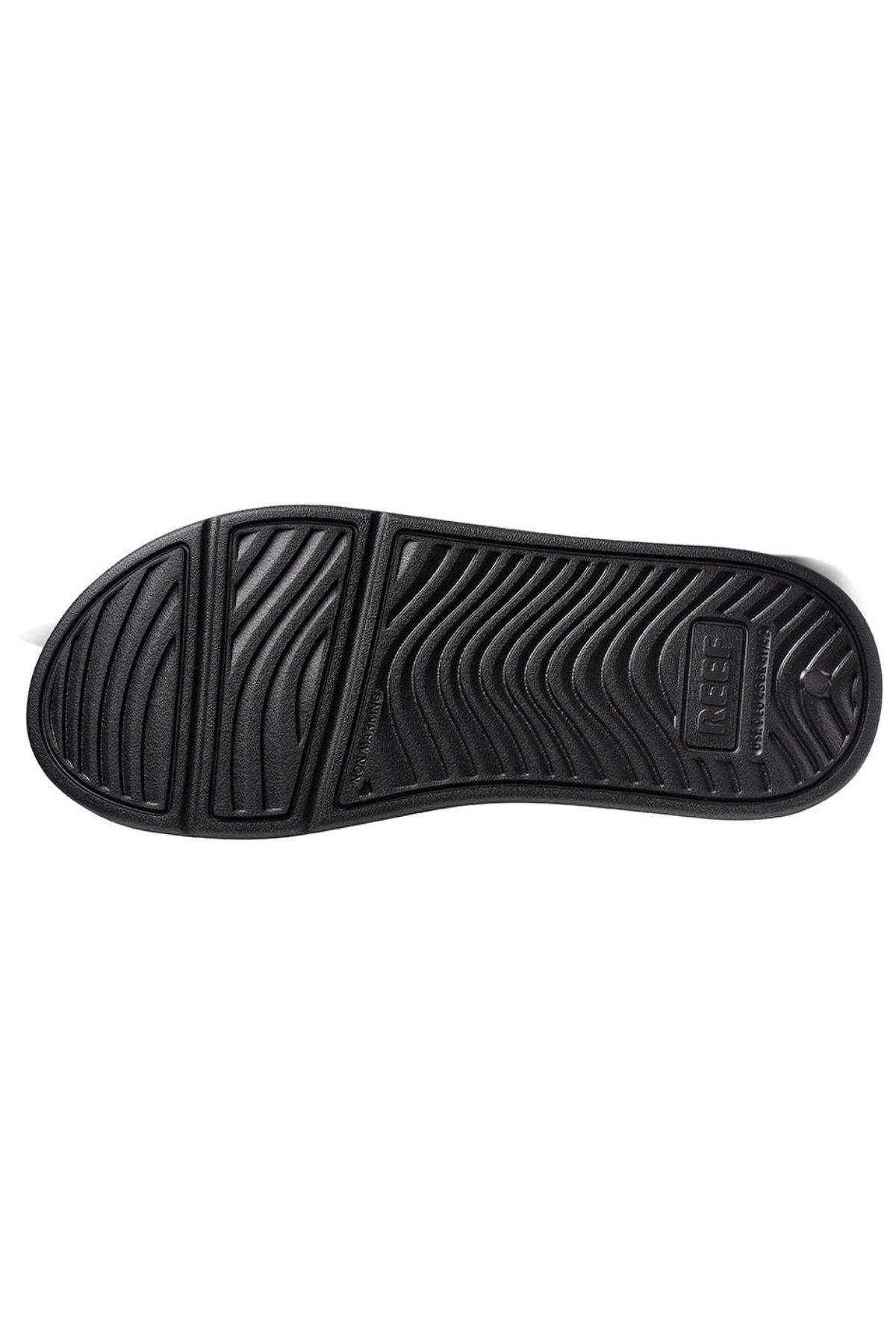 The image shows the black rubber sole of the REEF Oasis shoe with a textured pattern. The design includes wavy grooves and ridges for traction, providing excellent arch support. Made from renewable sugarcane EVA, the branding "OBER" is embossed on the heel area of the sole.