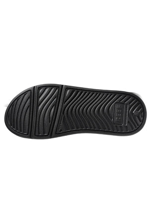 The image shows the black rubber sole of the REEF Oasis shoe with a textured pattern. The design includes wavy grooves and ridges for traction, providing excellent arch support. Made from renewable sugarcane EVA, the branding "OBER" is embossed on the heel area of the sole.