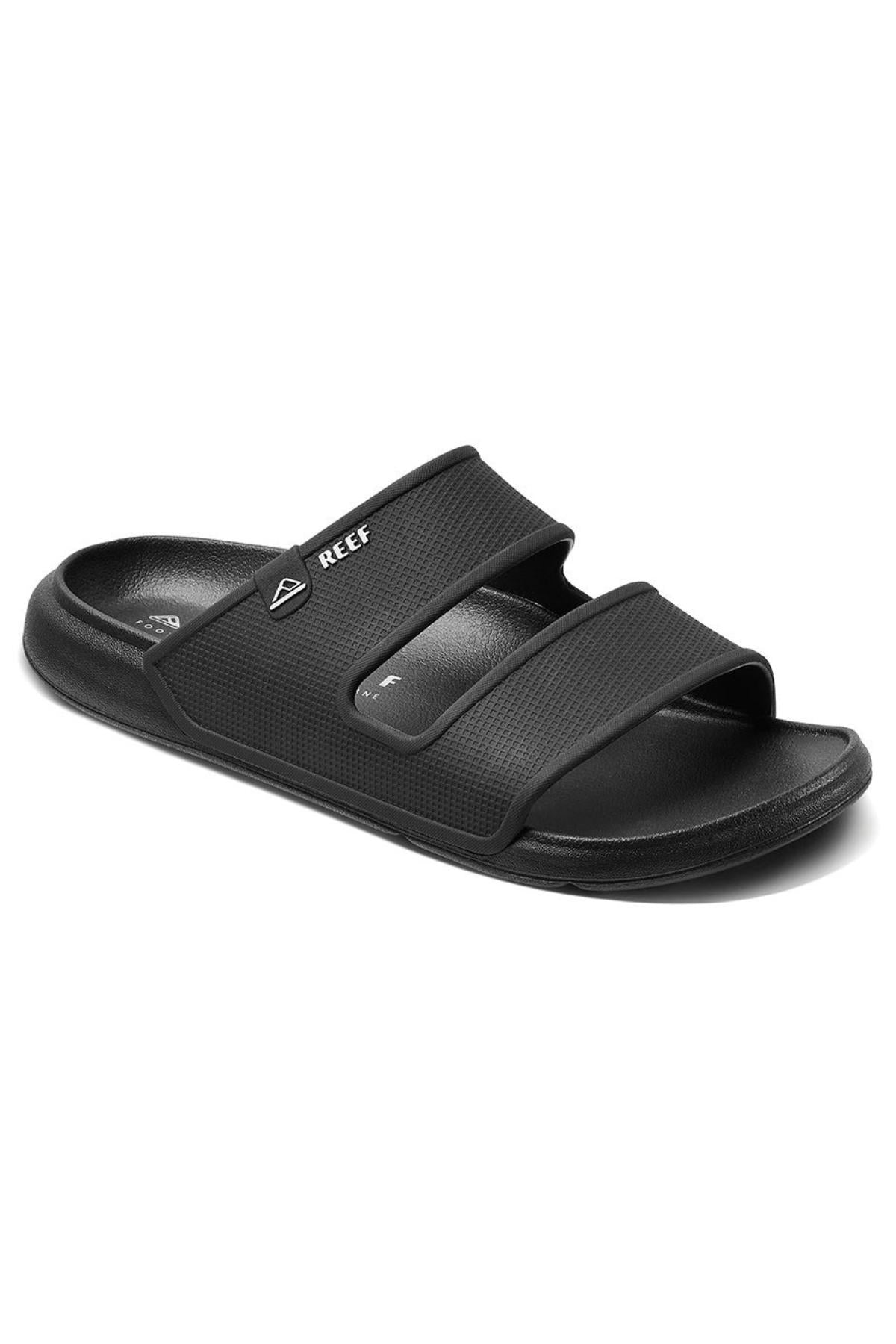 The REEF Oasis Double Up is a black slide sandal with dual straps displaying the "REEF" name and logo on the upper strap. It's water-friendly, has a textured footbed, flat sole, and provides excellent arch support for all-day comfort.
