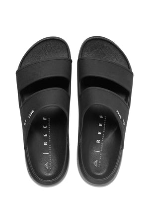 The REEF Oasis Double Up sandals are black slip-ons with dual wide foot straps, featuring "REEF" on the top strap. They offer a Cushion Lux insole with excellent arch support and are water-friendly, ensuring a sleek and stylish look when aligned side by side.
