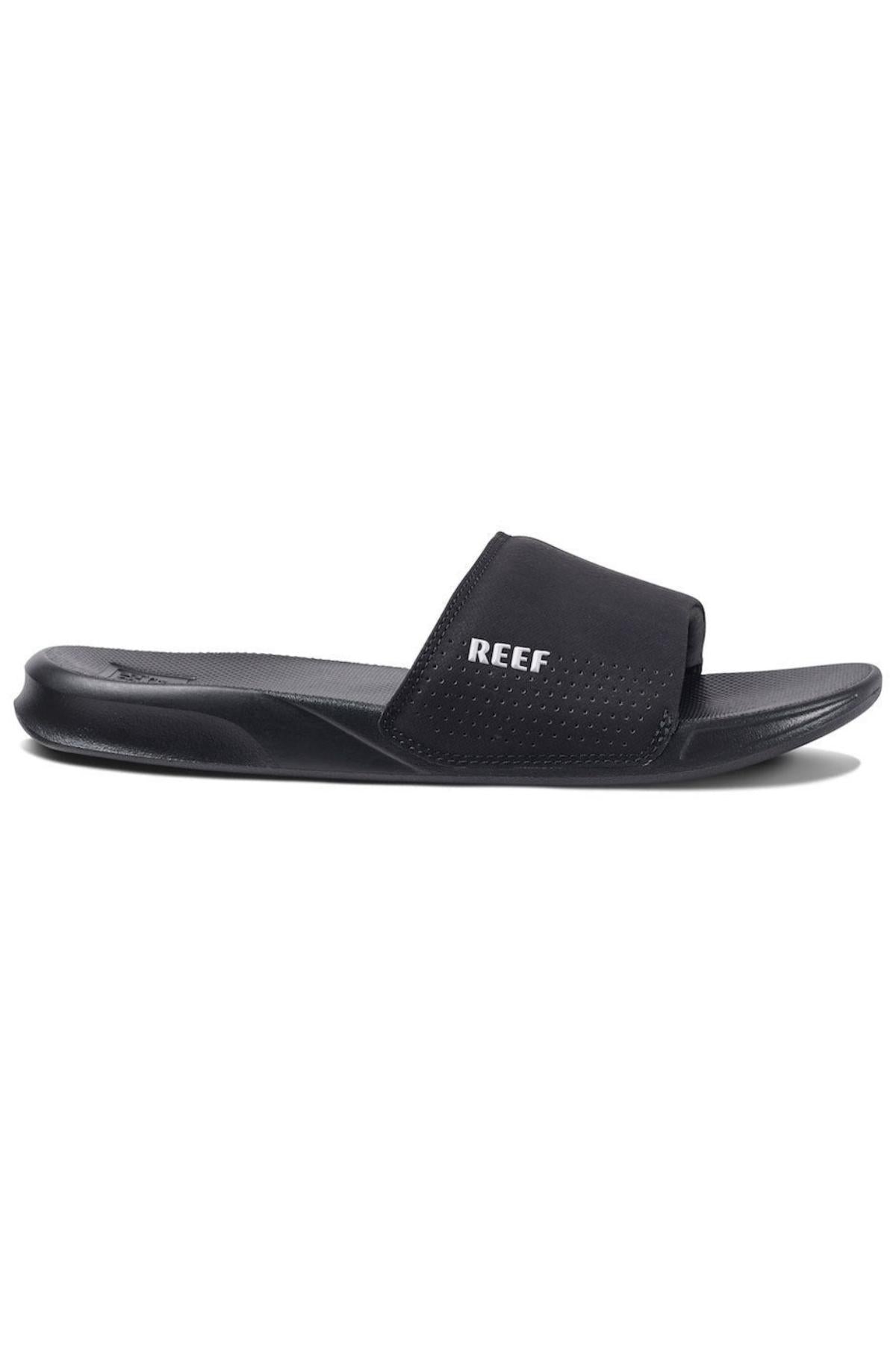 The REEF One Slide features a sleek, black design with a contoured footbed and wide strap across the top of the foot. The strap has small perforations for ventilation and proudly displays the white "REEF" logo. These stylish slides offer modern comfort with a waterproof design, perfect for versatile wear.