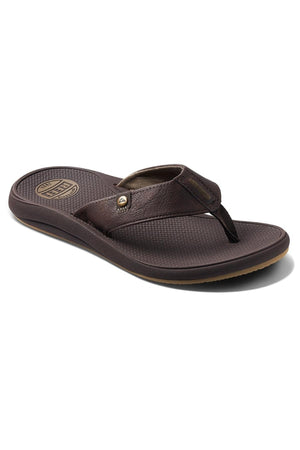 A single REEF Phantom Nias flip-flop sandal, crafted from brown leather, features a textured insole and an emblem on the heel area. It offers superior traction, a wide strap with a small metal detail, and a dark footbed with slight elevation at the heel for enhanced comfort.