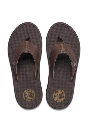 A bird's-eye view of the REEF Phantom Nias flip-flops, showcasing their textured sole and thick straps for a comfortable fit and superior traction. The insoles are printed with the brand name "Reef" and the year "1984," while a small logo tag adorns the straps.