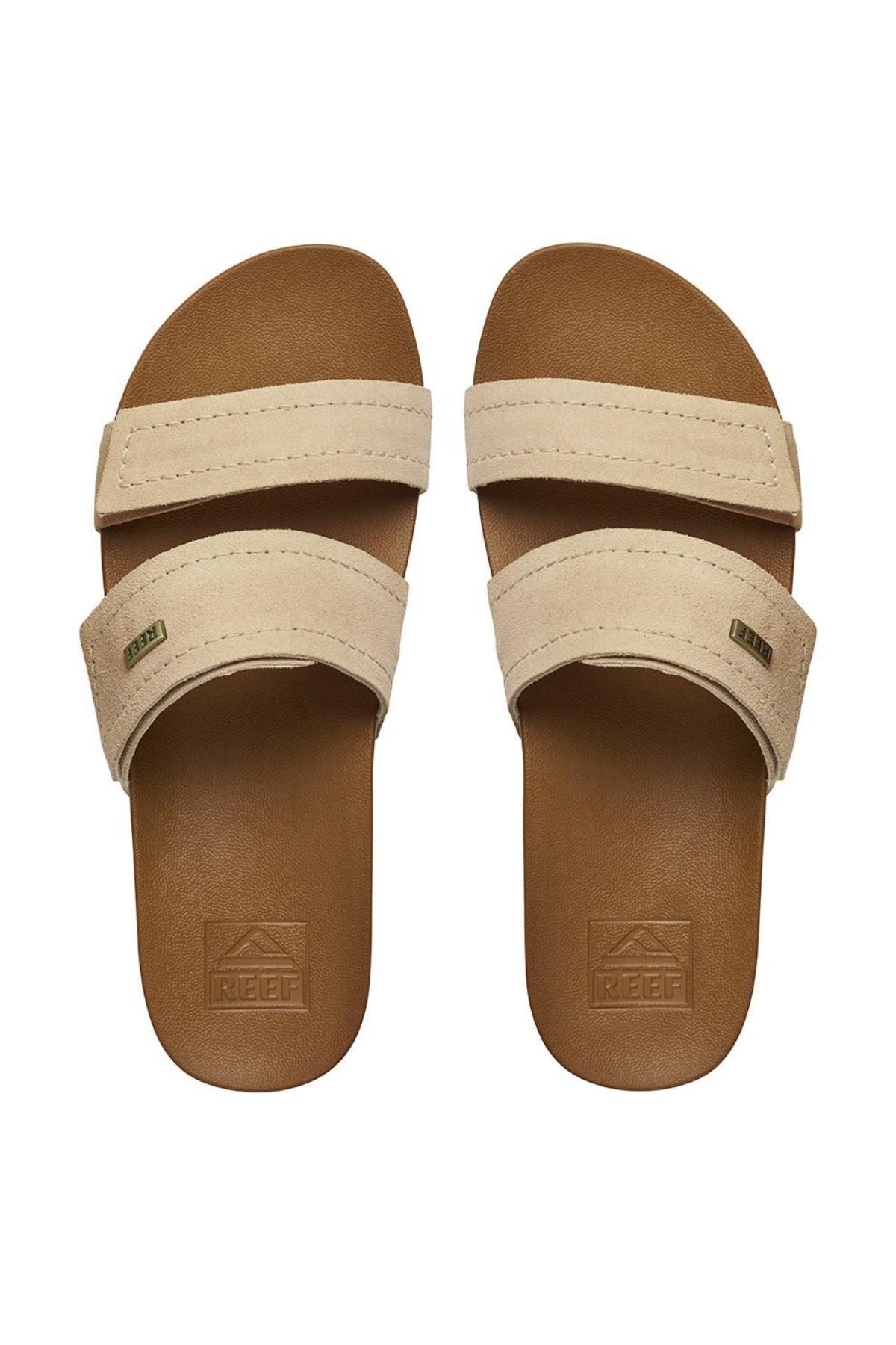 The REEF Velcro Vista SE are tan slide sandals with premium leather straps, a brown footbed with cushion bounce midsole, "Reef" embossed on the footbed, and a small label on the straps. They are viewed from above.