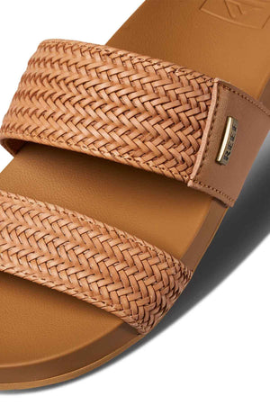 Close-up of the eco-friendly REEF Vista Braid II sandal with a woven texture on the wide strap, a metal tag on the side, and its cushioned midsole accentuating a slightly darker smooth footbed.