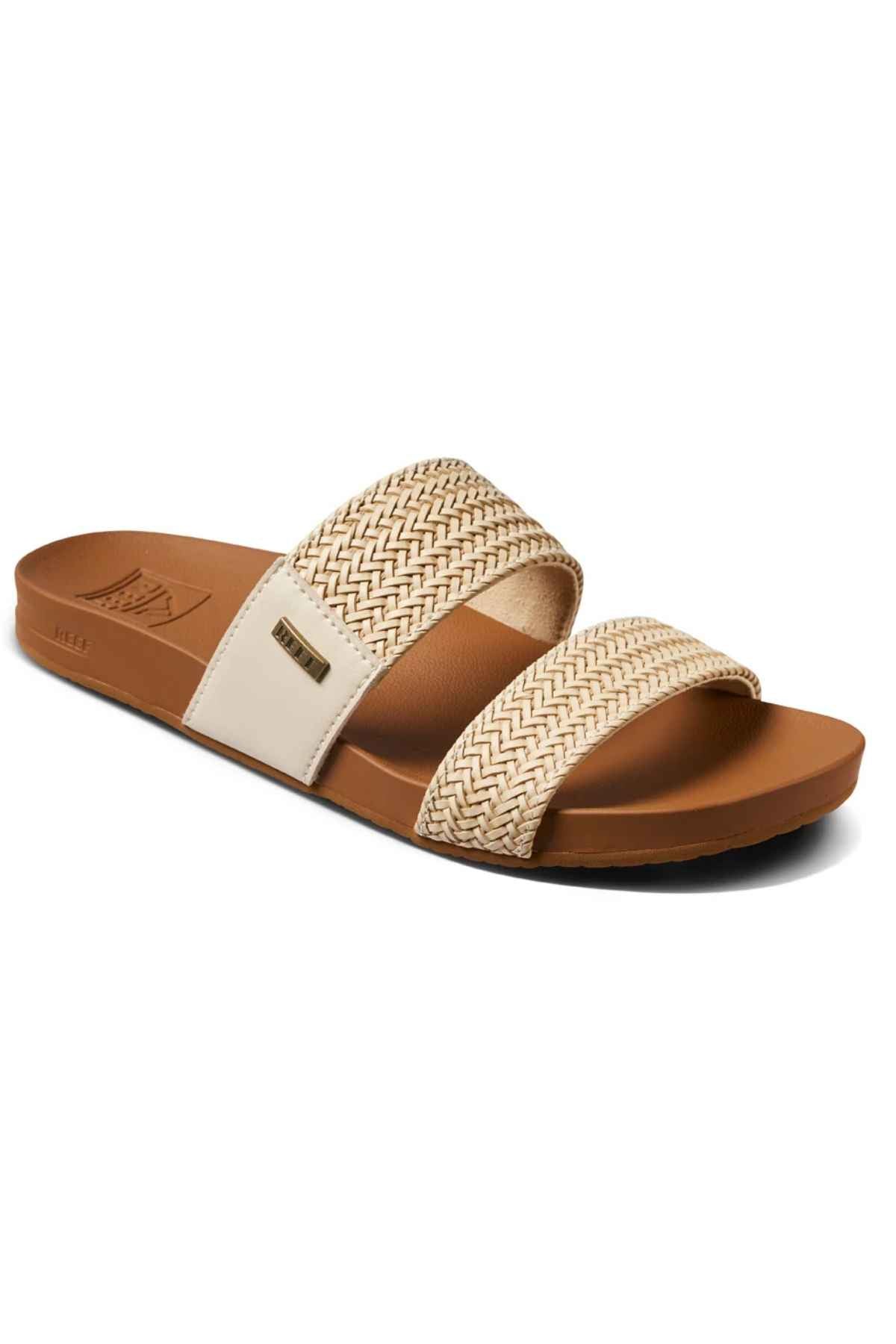 The REEF Vista Braid II is an eco-friendly tan slide sandal with a flat sole, two wide cream and tan woven straps, a cushioned midsole, and a small metallic logo on the outer side.