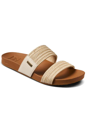 The REEF Vista Braid II is an eco-friendly tan slide sandal with a flat sole, two wide cream and tan woven straps, a cushioned midsole, and a small metallic logo on the outer side.
