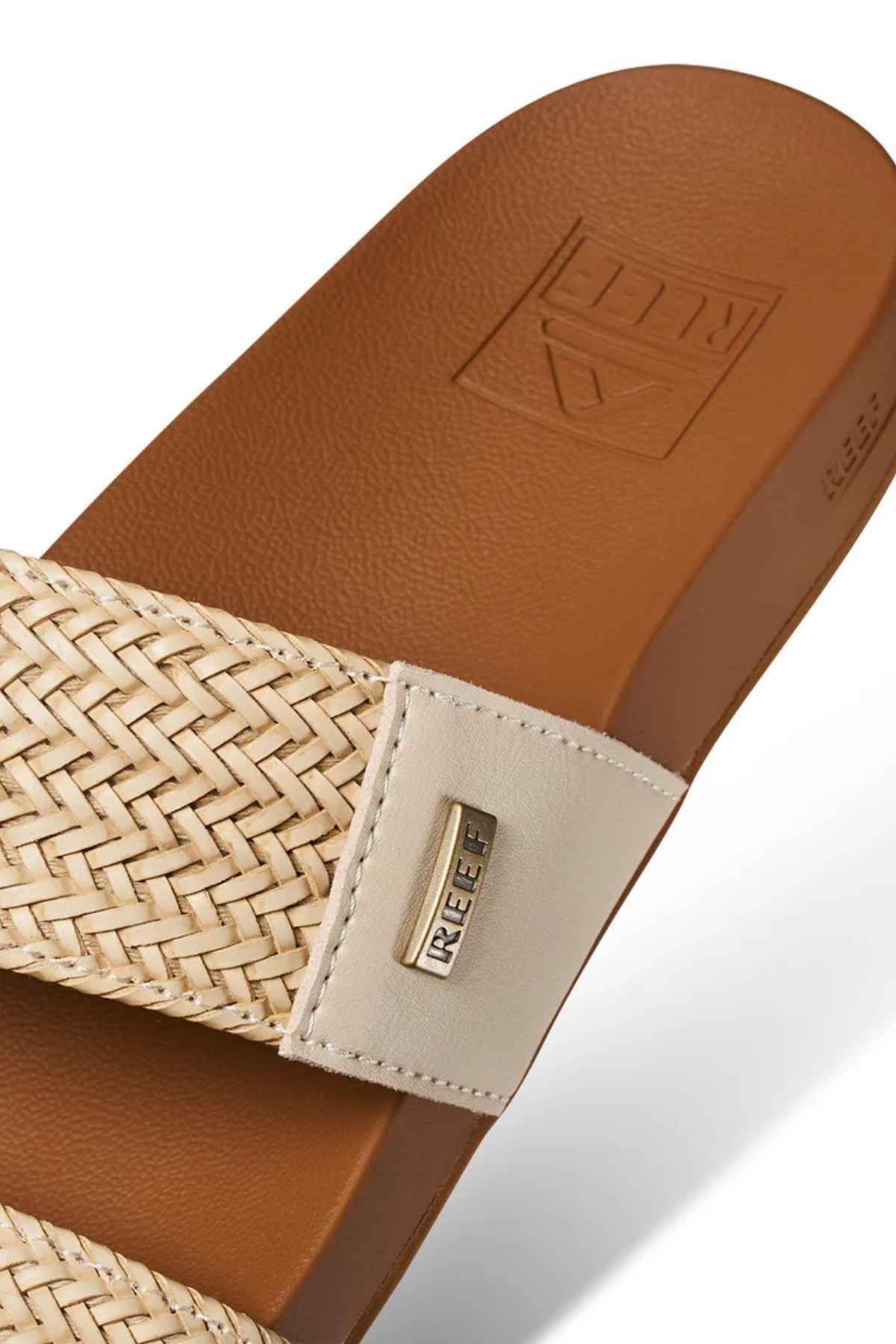 Close-up of the REEF Vista Braid II sandal featuring a tan woven strap, beige leather accent with metallic REEF logo, embossed footbed, and cushioned eco-friendly midsole for all-day comfort.