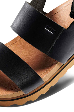Close-up of the black REEF Vista Hi Buckle vegan leather sandal with two wide straps, a tan cushioned footbed, and a thick light brown sole with wavy tread. Part of the logo appears on the upper strap, showcasing these stylish sandals.