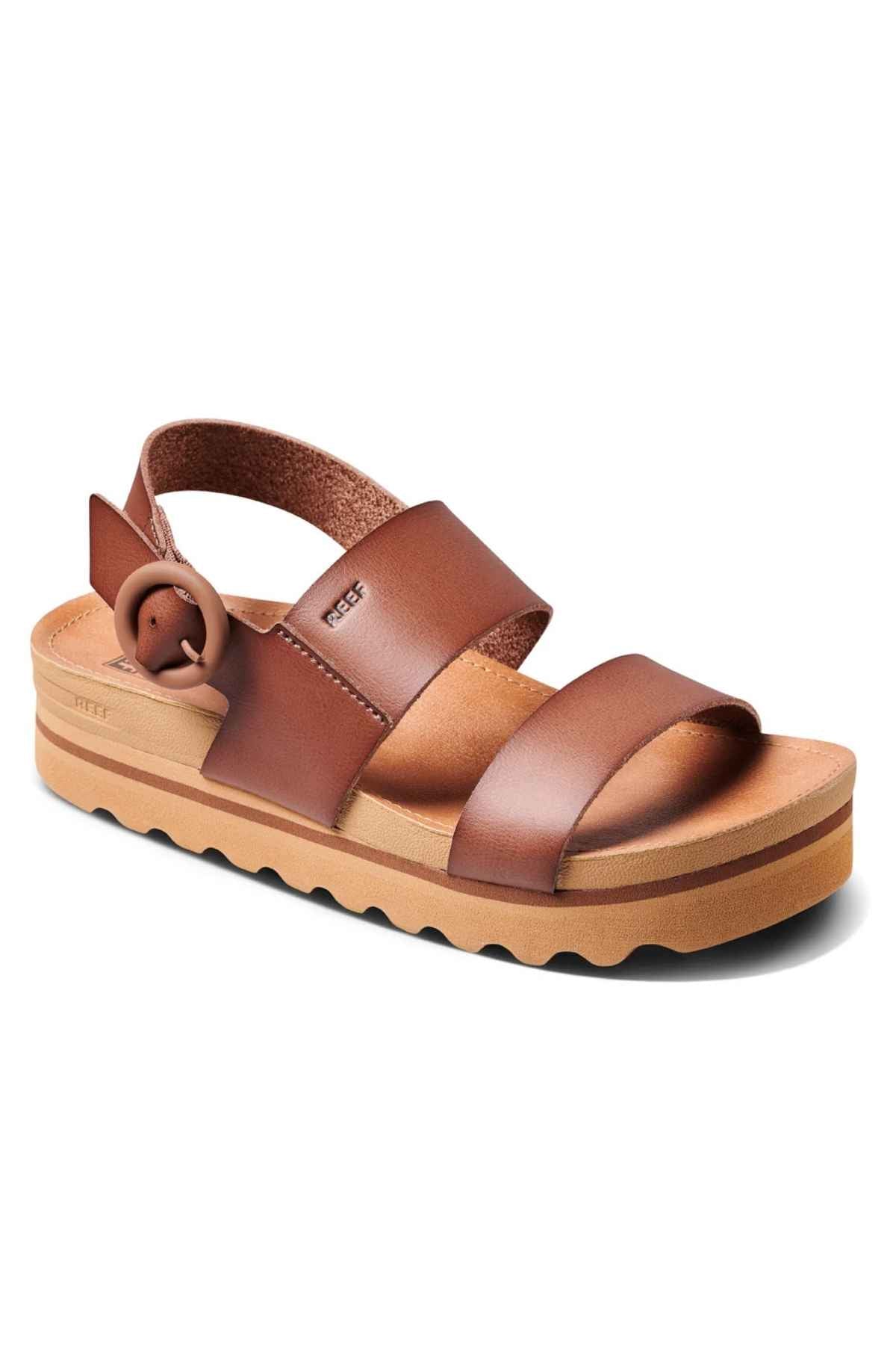 The REEF Vista Hi Buckle is a fashionable platform sandal designed with vegan leather straps, featuring a thick sole, two wide front straps, and an adjustable back strap adorned with a round buckle. Its textured platform enhances height and adds a chic touch.