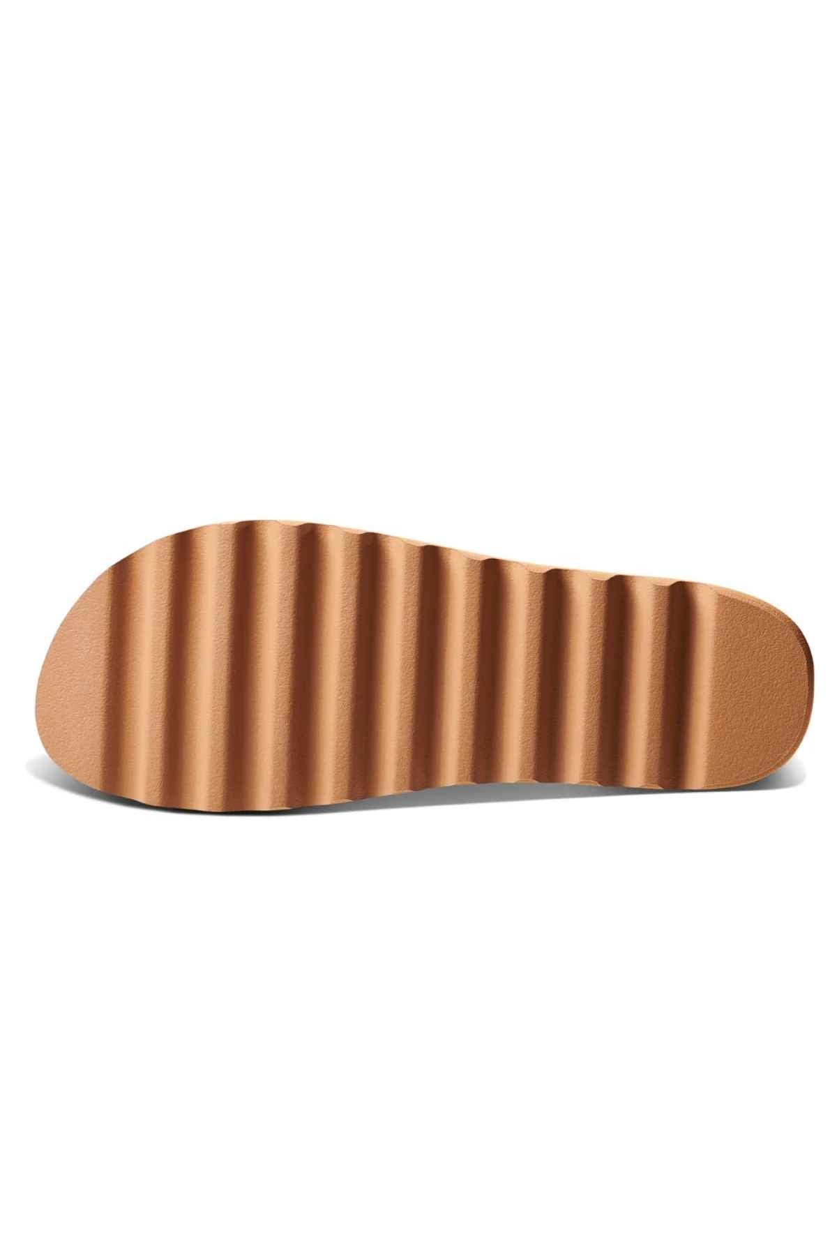 The image showcases the sole of a REEF Vista Hi Buckle sandal, highlighting its wavy, ribbed texture. This platform sandal features a brown sole with a sleek finish, enhanced by sophisticated vegan leather straps.