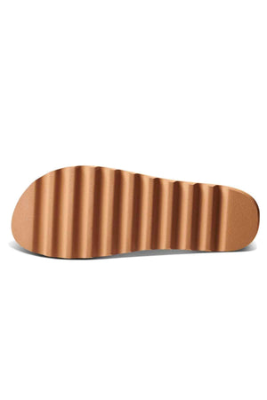The image showcases the sole of a REEF Vista Hi Buckle sandal, highlighting its wavy, ribbed texture. This platform sandal features a brown sole with a sleek finish, enhanced by sophisticated vegan leather straps.