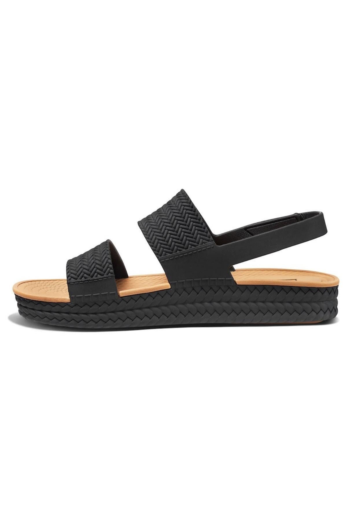 Side view of the REEF Water Vista sandal in black, featuring two woven straps and an elastic heel strap. Designed with arch support, it has a tan sole on a textured black platform base, offering style and comfort.