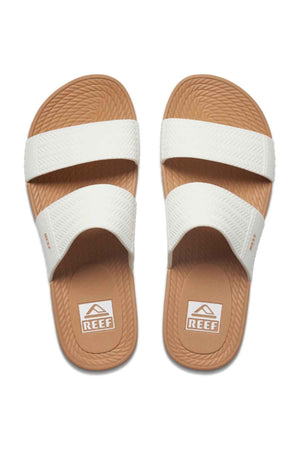 The REEF Water Vista Slide features wide white straps, textured brown soles, and dual-density EVA footbeds with the "REEF" logo. The tan slide sandals are displayed side by side from a top view.