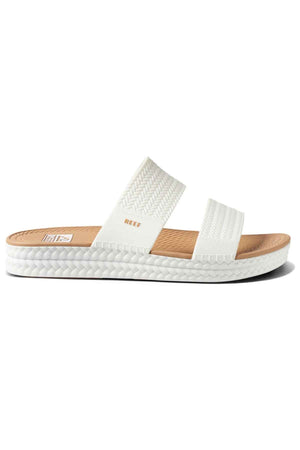 The REEF Water Vista Slide is a white sandal featuring two textured straps, a tan dual density EVA footbed, a white sole with textured edging, and the “REEF” logo on the upper strap.