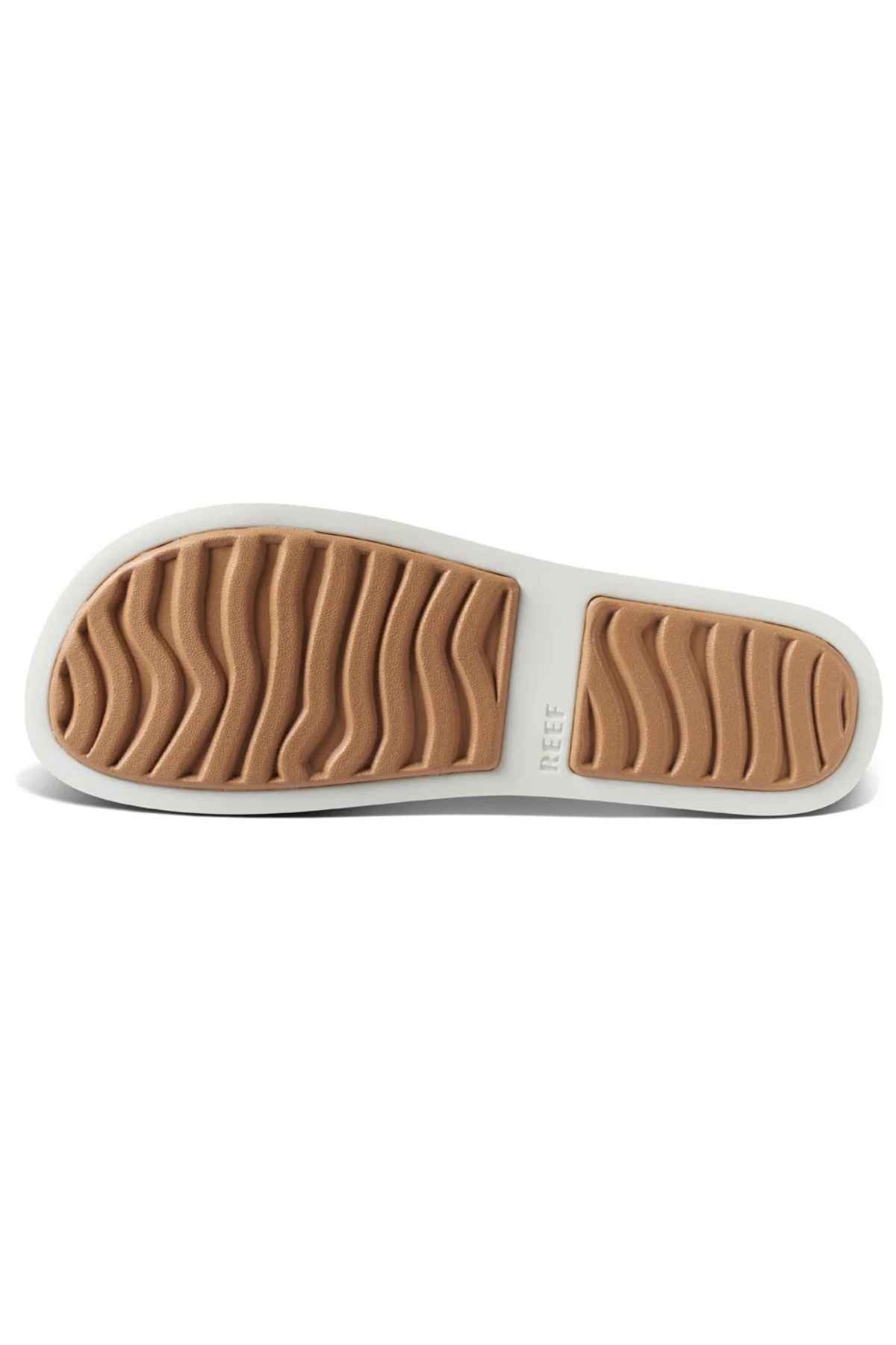 The image shows the bottom view of a REEF Water Vista Slide sandal with a white outer edge, light brown rubber tread featuring wavy grooves for traction, and "REEF" near the heel, highlighting its dual density EVA footbed.
