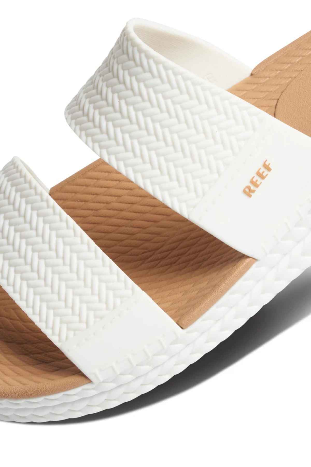 Close-up of a REEF Water Vista Slide sandal in white with a woven texture, two thick straps, gold "REEF" branding, and a light brown dual-density EVA footbed featuring a textured pattern for comfort.