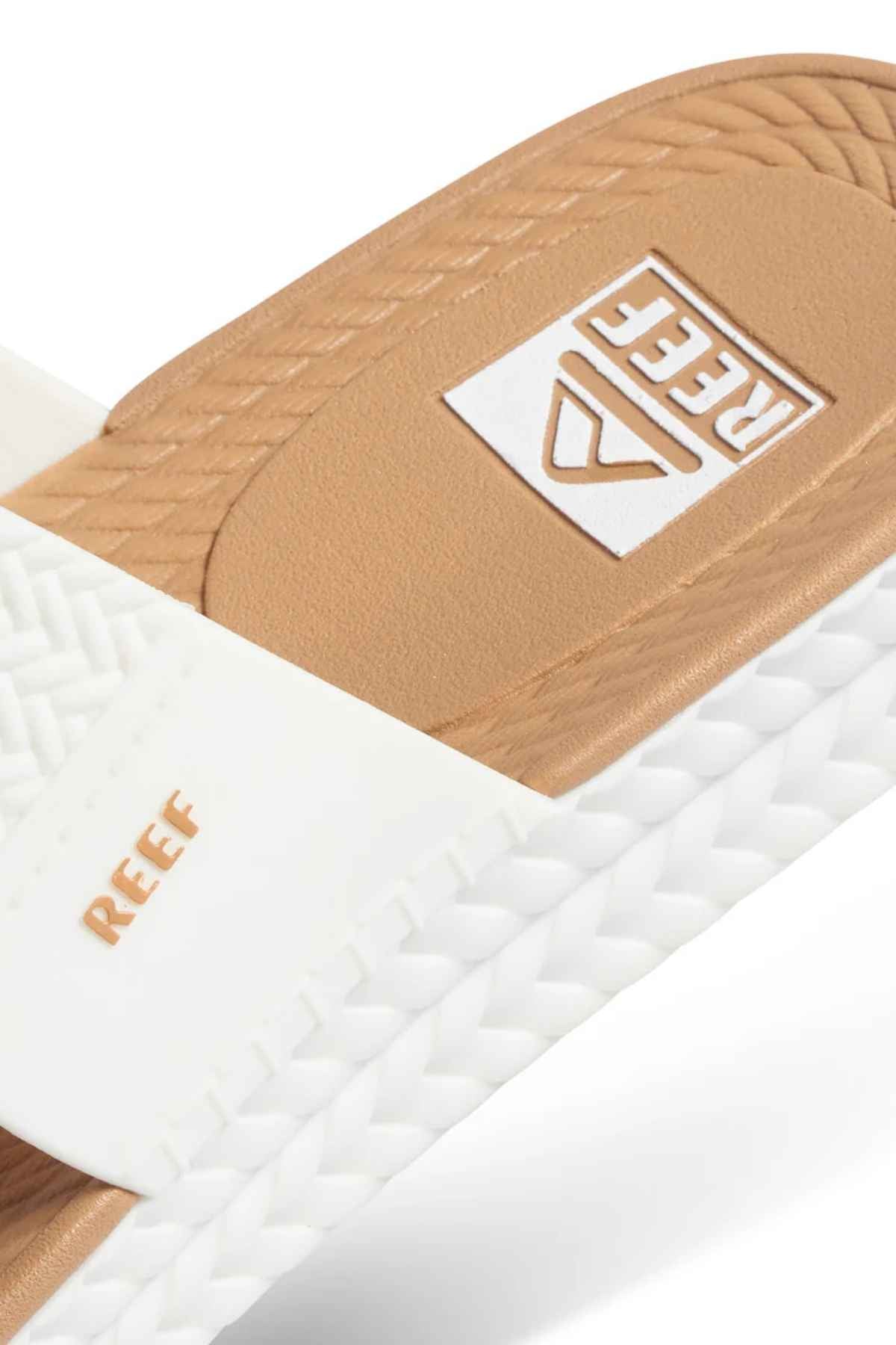 Close-up of a white and tan REEF Water Vista Slide with the REEF logo on the strap and footbed, dual-density EVA footbed, textured sole, and woven design detail.