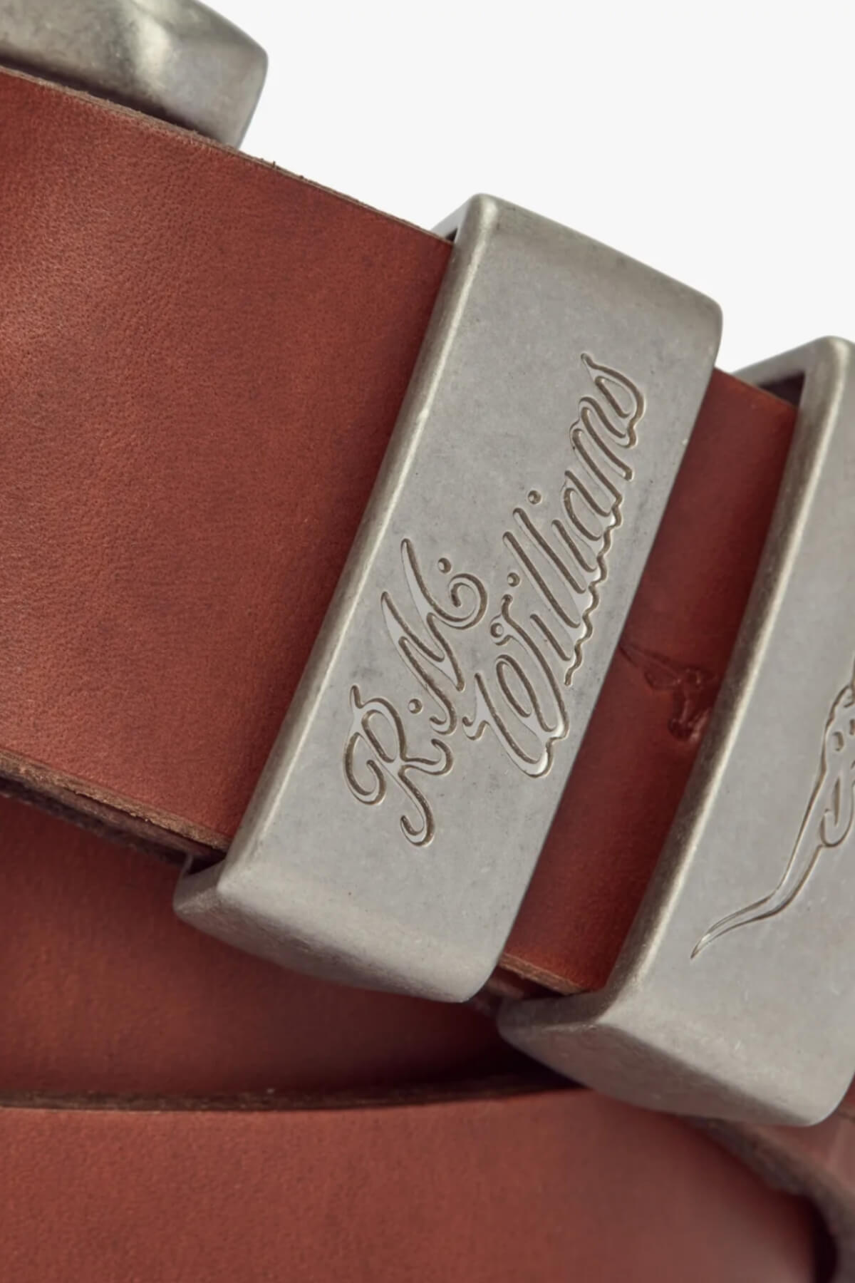 Close-up of the RM Williams 1 1/2 3 Piece Solid Hide Belt, featuring a brown leather strap and brushed nickel buckle engraved with "R.M. Williams." Made in Australia, the buckle's reflective metallic finish complements the leather.